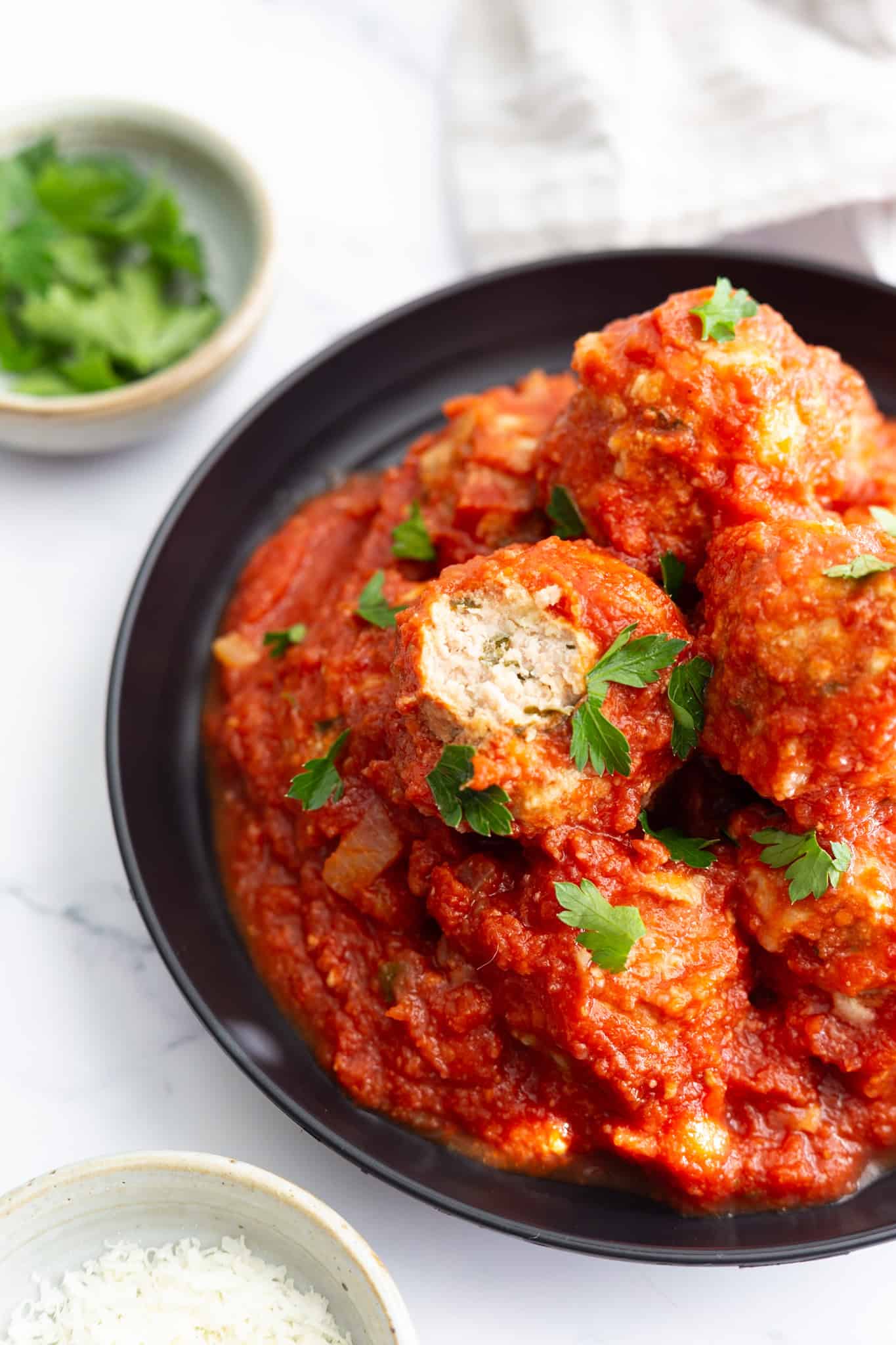 A plate of Italian meatballs in marinara sauce with a piece cut out of one of them. 