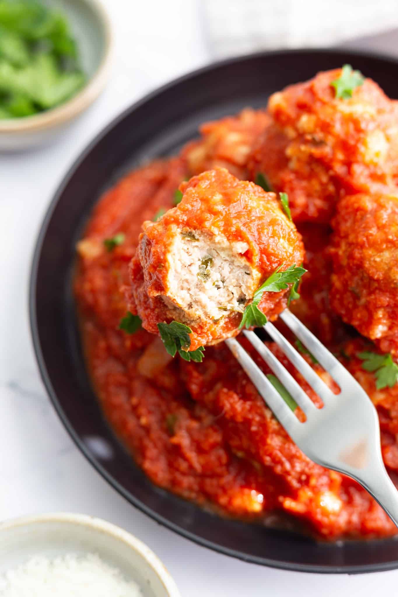 A fork inserted into an Italian meatball, with a piece cut out to show the interior.