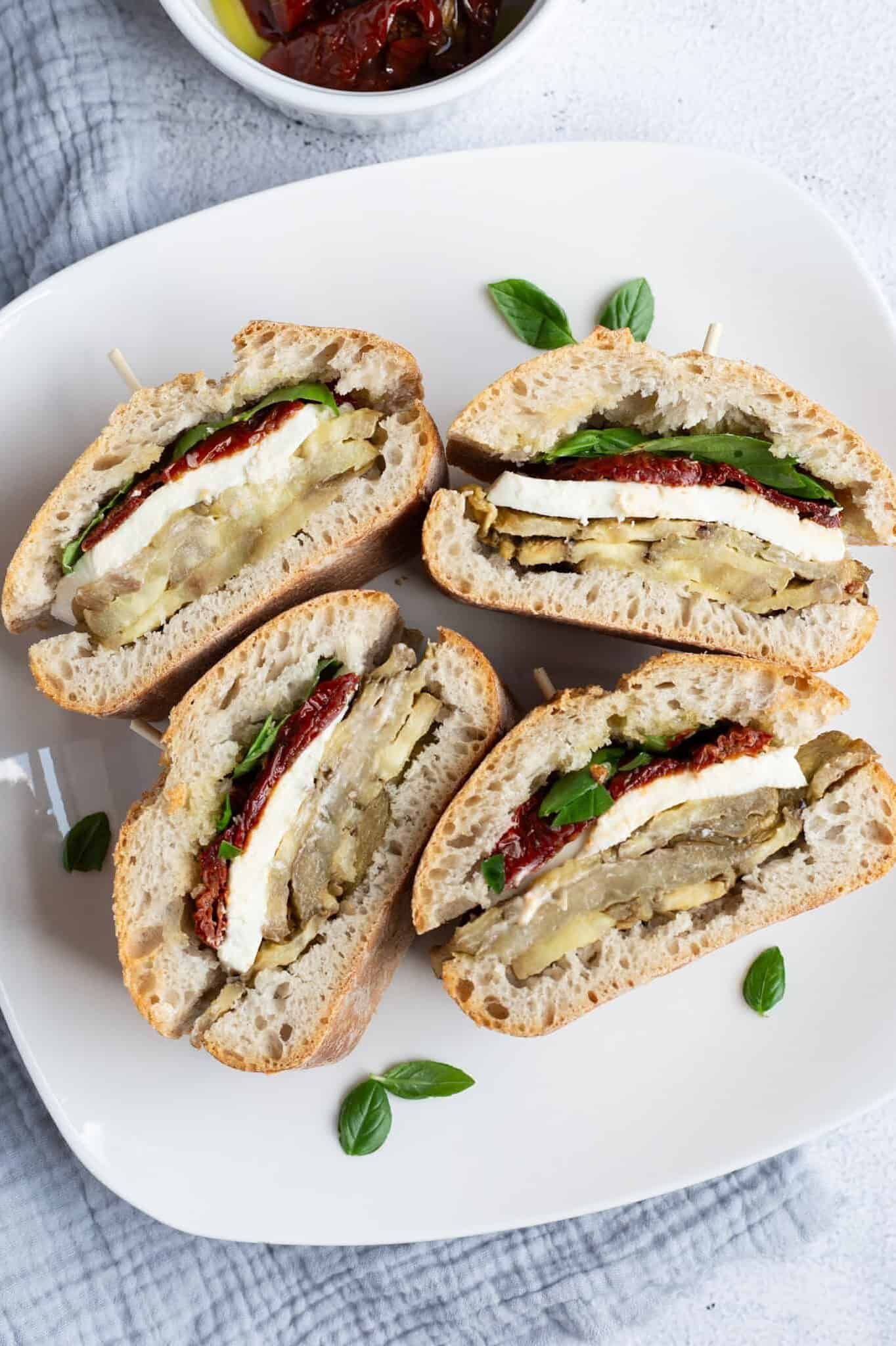 A plate of four eggplant and mozzarella sandwiches.