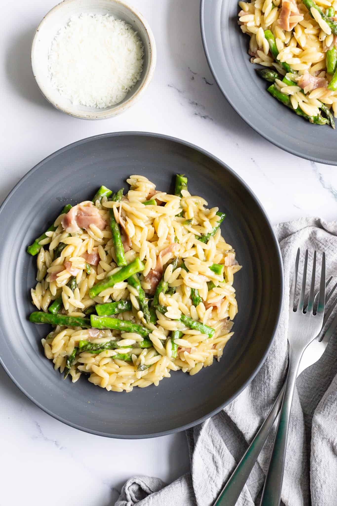A grey plate of orzo with asparagus and Parmesan with bits of torn prosciutto.