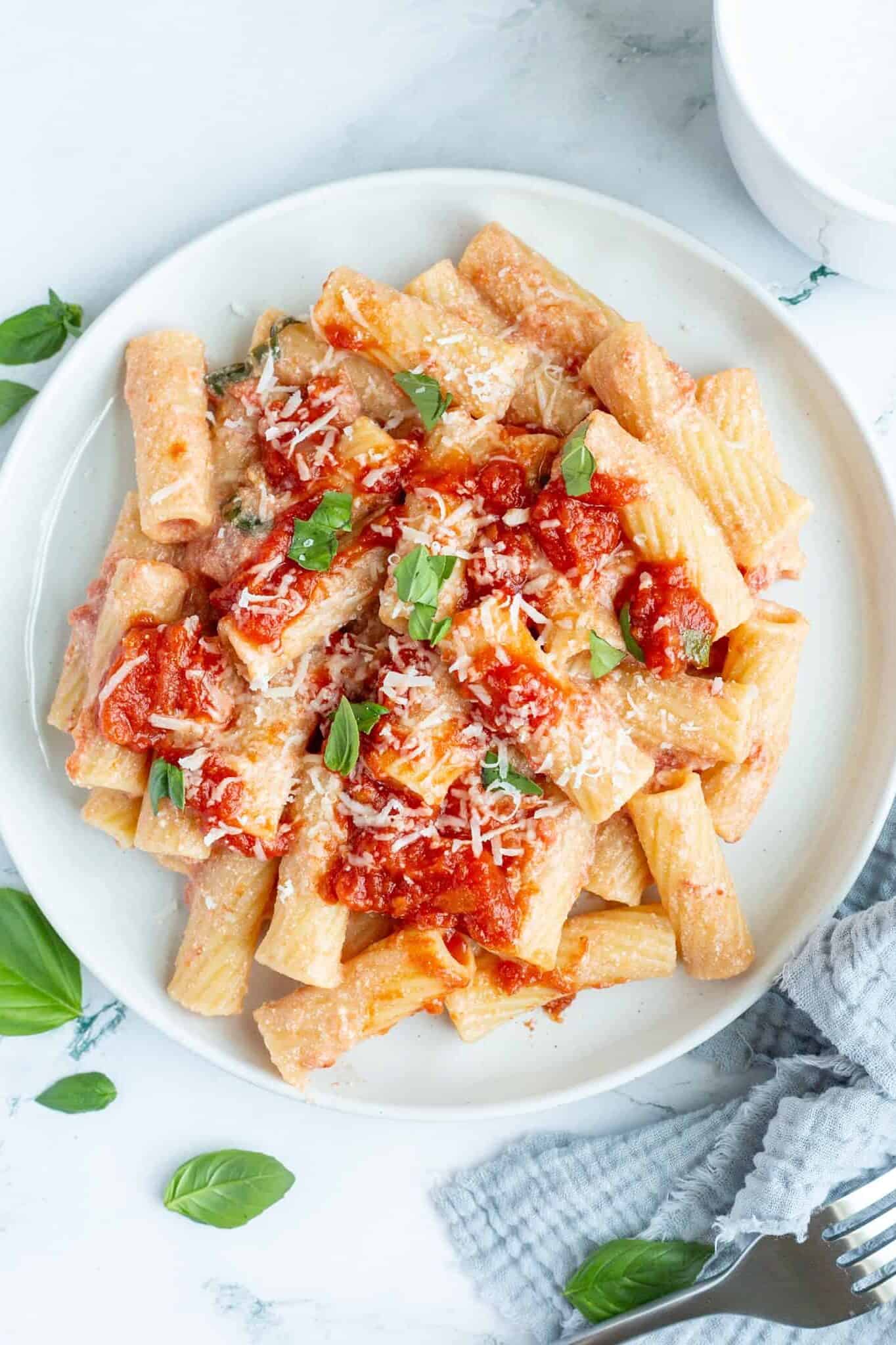 A white plate containing pasta with ricotta cheese and surrounded by torn fresh basil.