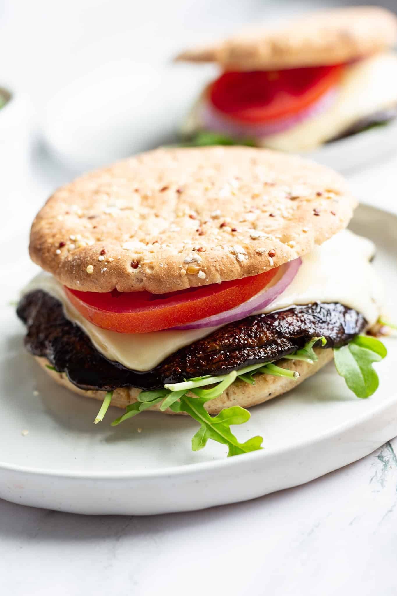 A grilled portobello burger topped with sliced tomato, sliced red onion, and melted baby Swiss on a bed of arugula and between two sandwich buns.