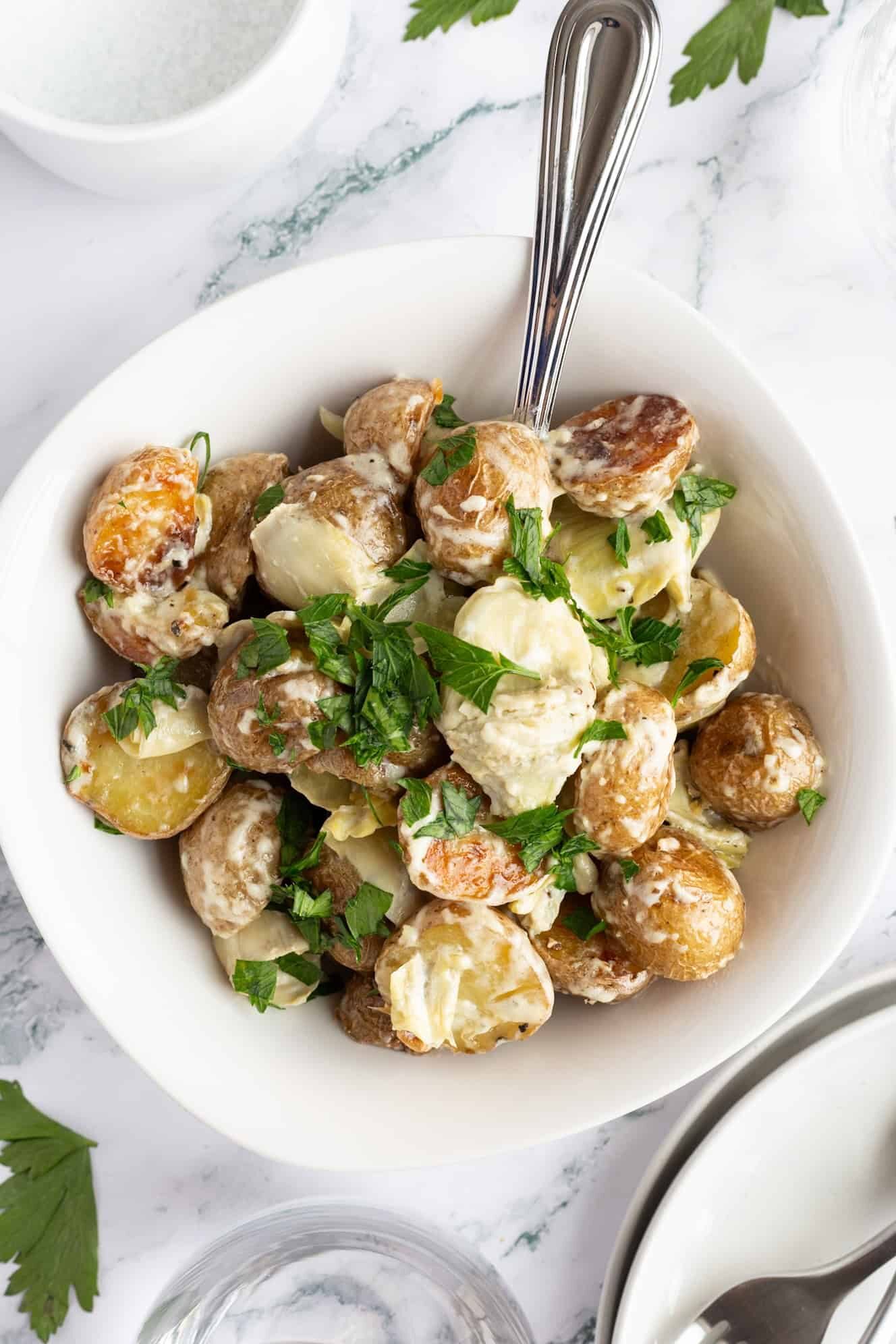 A bowl of potatoes and artichokes with a serving spoon sticking from it.