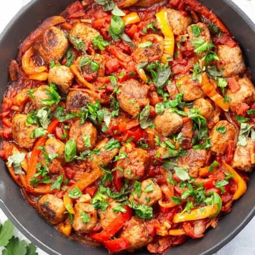 A large skillet of Italian sausage and peppers, garnished with fresh parsley.