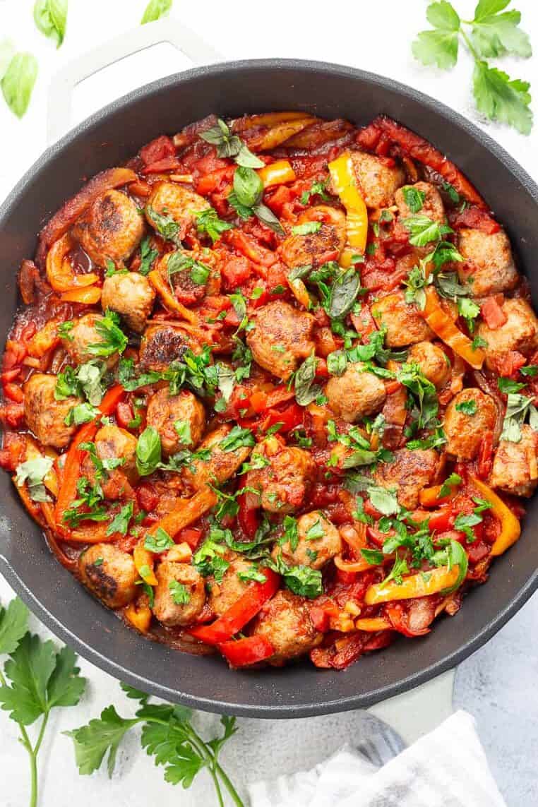 A large skillet of Italian sausage and peppers, garnished with fresh parsley.