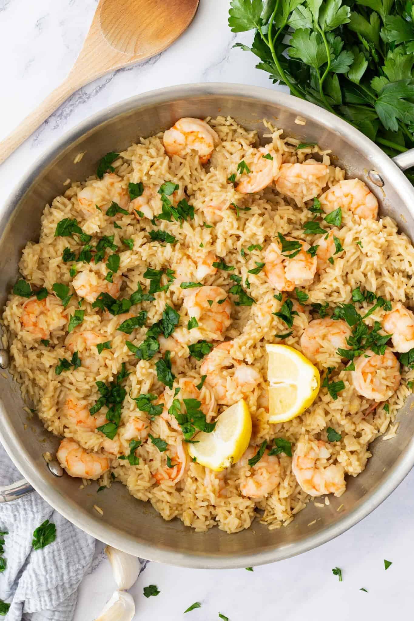 A pan filled with basmati rice and shrimp and garnished with parsley and lemon wedges.