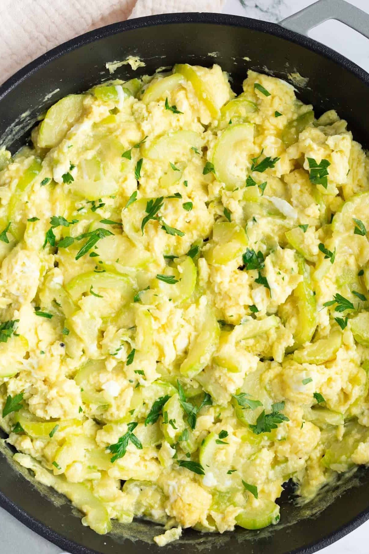 A skillet of cooked zucchini and scrambled eggs, garnished with minced fresh parsley.