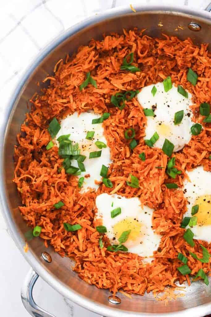 A pan of shredded sweet potatoes with chorizo and eggs and garnished with scallions.