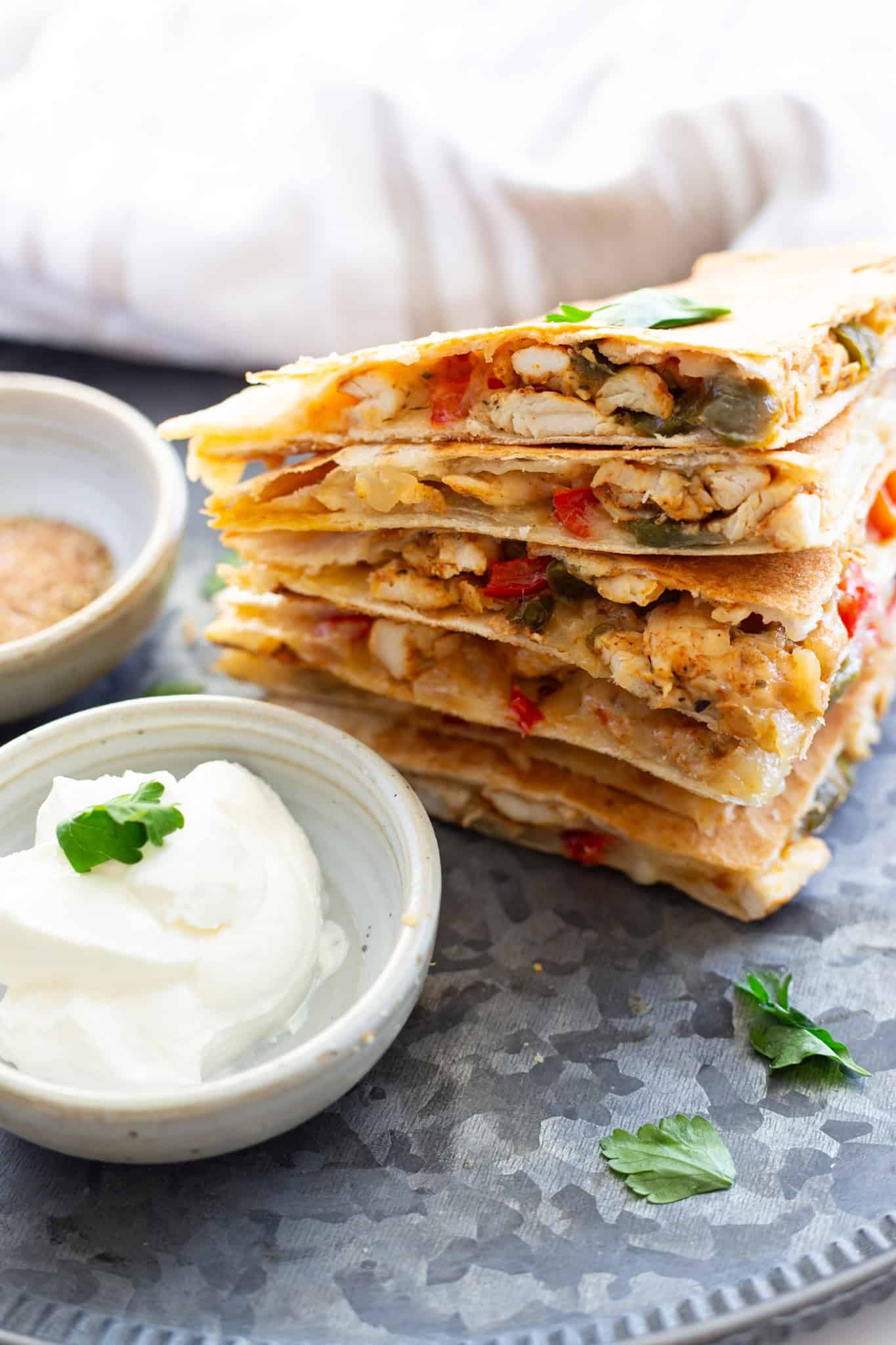 A stack of chicken quesadillas next to a bowl of sour cream for dipping.
