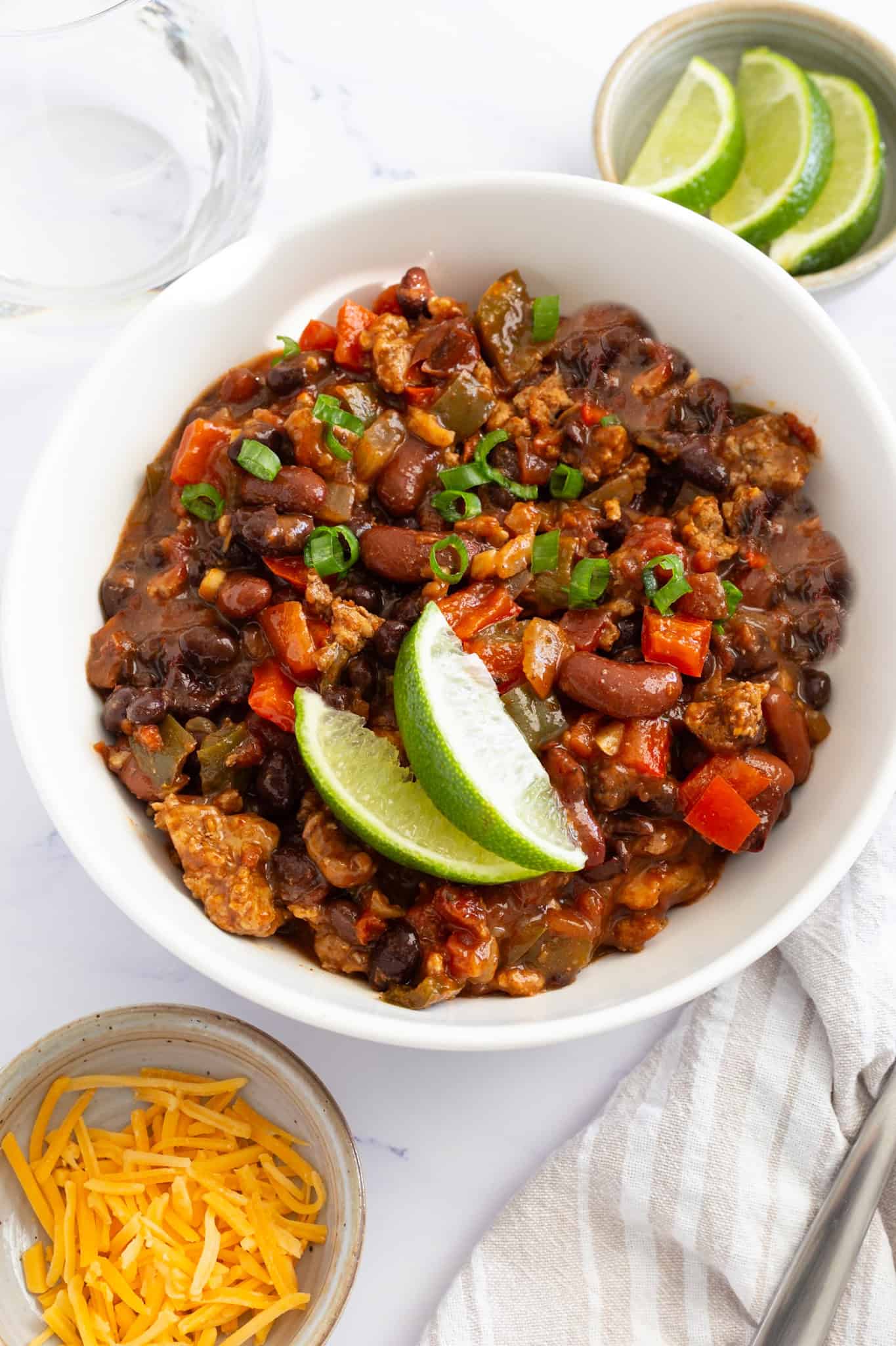 A bowl of ground chicken chili garnished with lime wedges and sliced scallions.