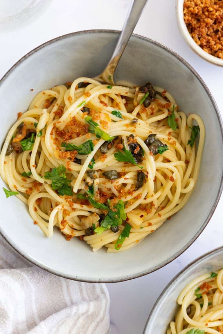 Two bowls of pasta with capers and roasted garlic, garnished with fresh parsley.