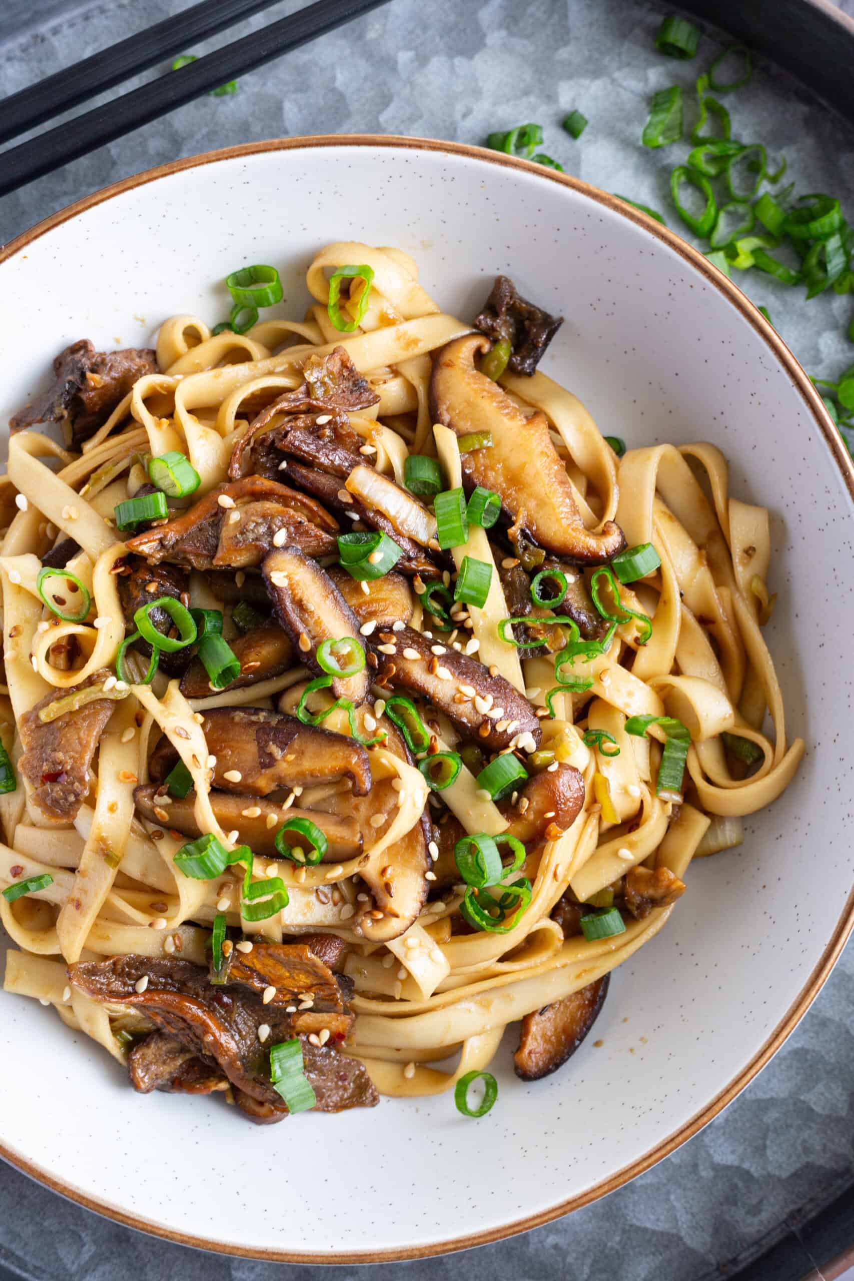 A bowl of shiitake mushroom noodles, garnished with scallions and toasted sesame seeds.