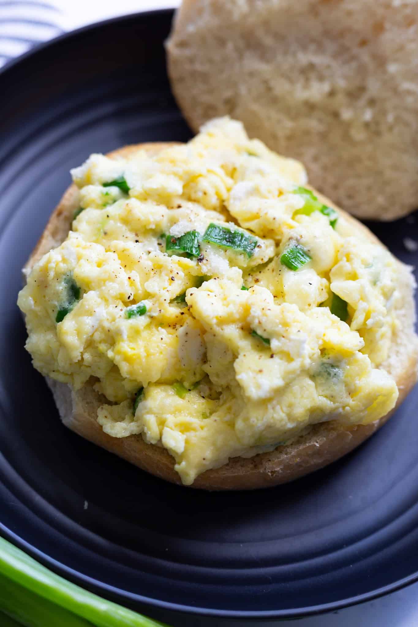 A bottom roll topped with eggs and melted mozzarella, with the top bun laying beside it.