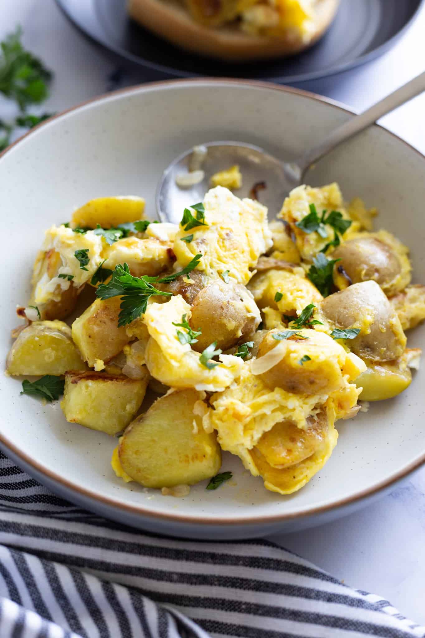 A bowl of potatoes and eggs with a serving spoon.