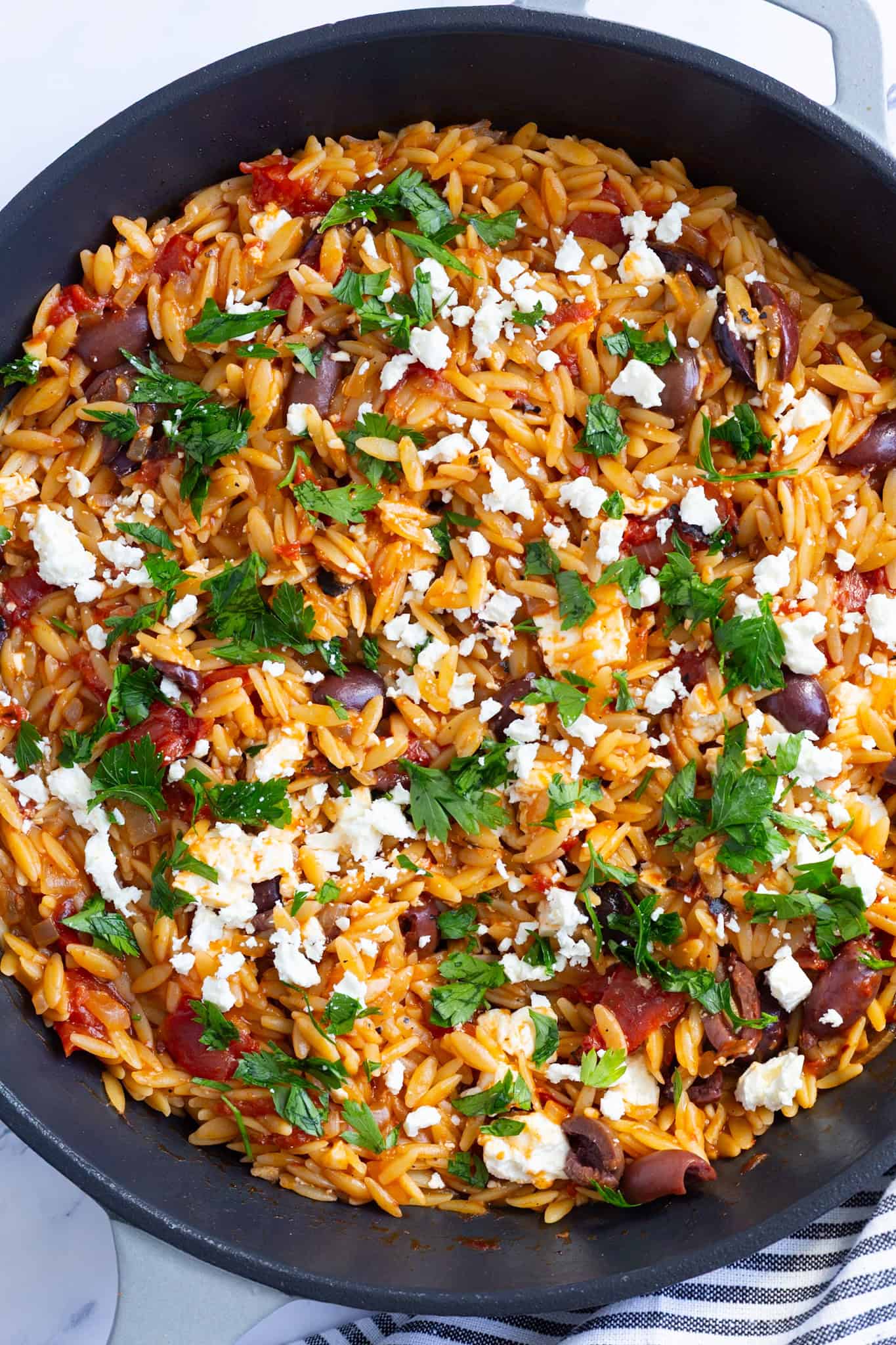 A pan filled with orzo cooked with fire-roasted tomatoes and topped with olives and feta.