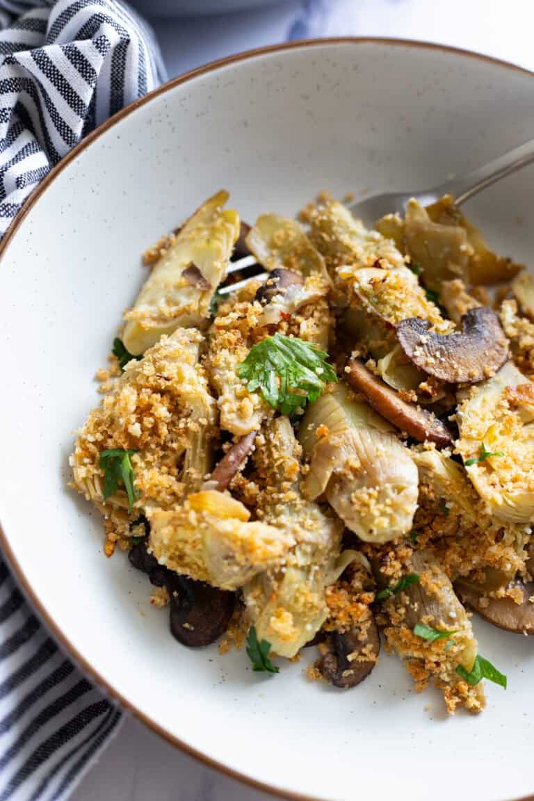 A bowl of artichoke hearts with mushrooms and Parmesan breadcrumbs.