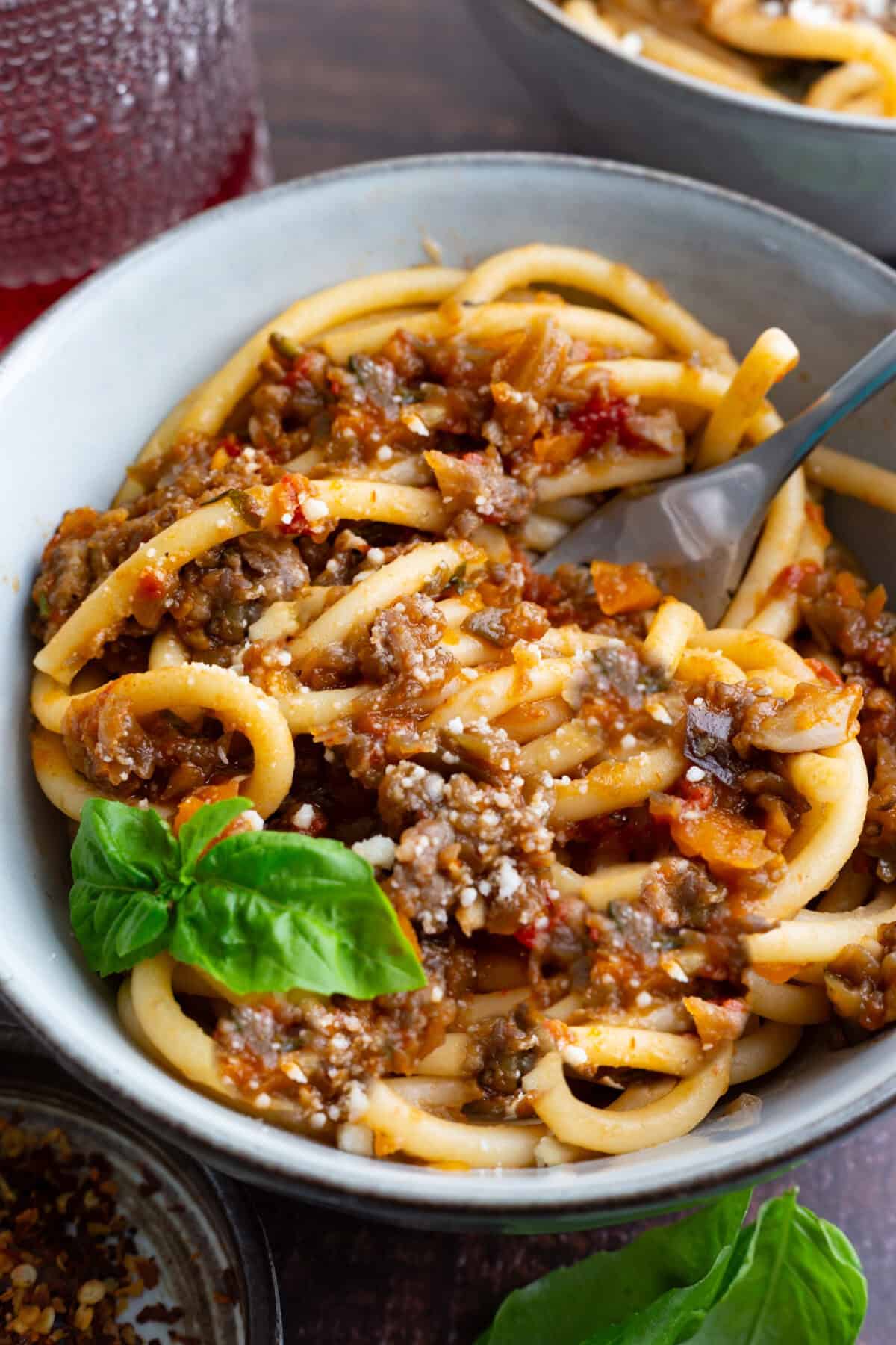 A bowl of bucatini bolognese with veggies and sausage.